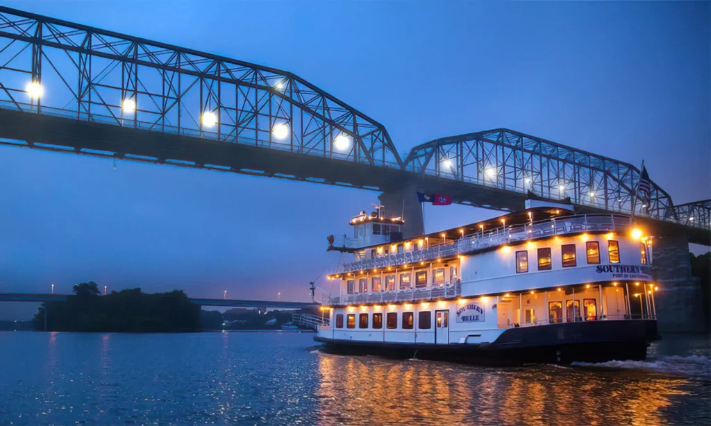 The Southern Belle riverboat gliding under a bridge lilt up with lights