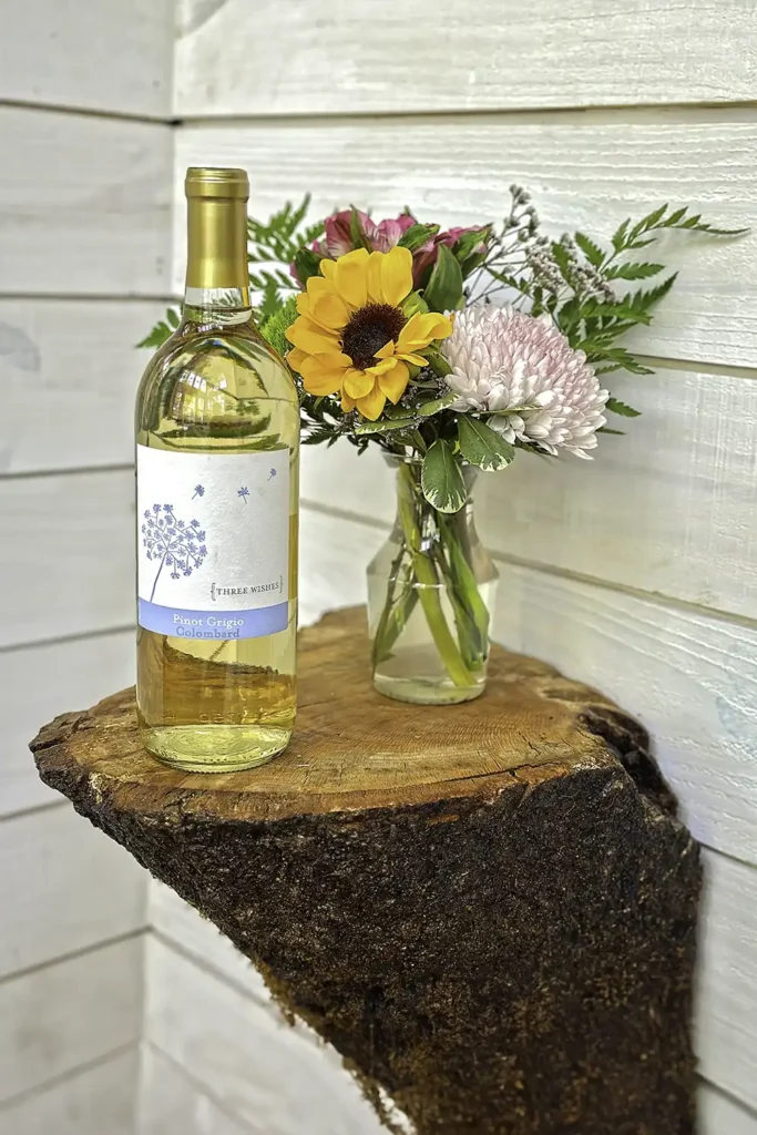 Bottle of white wine on a tree stump table next to a vase of colorful flowers