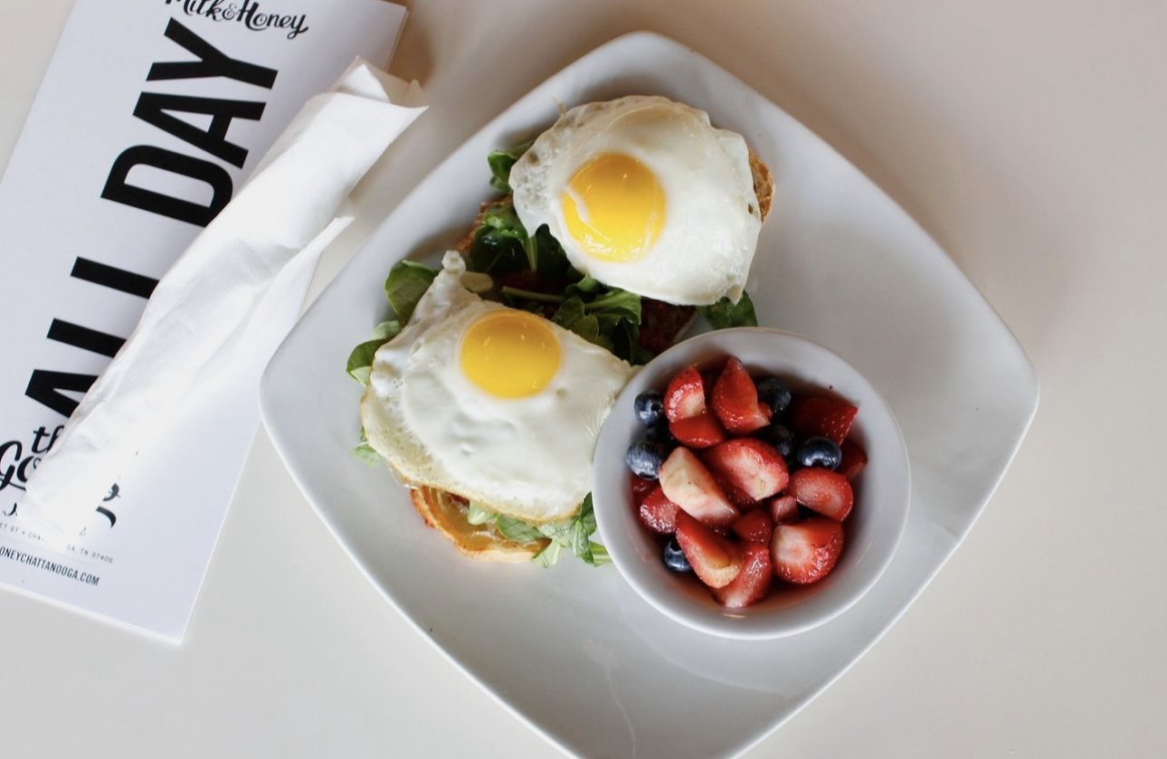 two over easy eggs on a white plate next to a bowl of strawberries and blueberries
