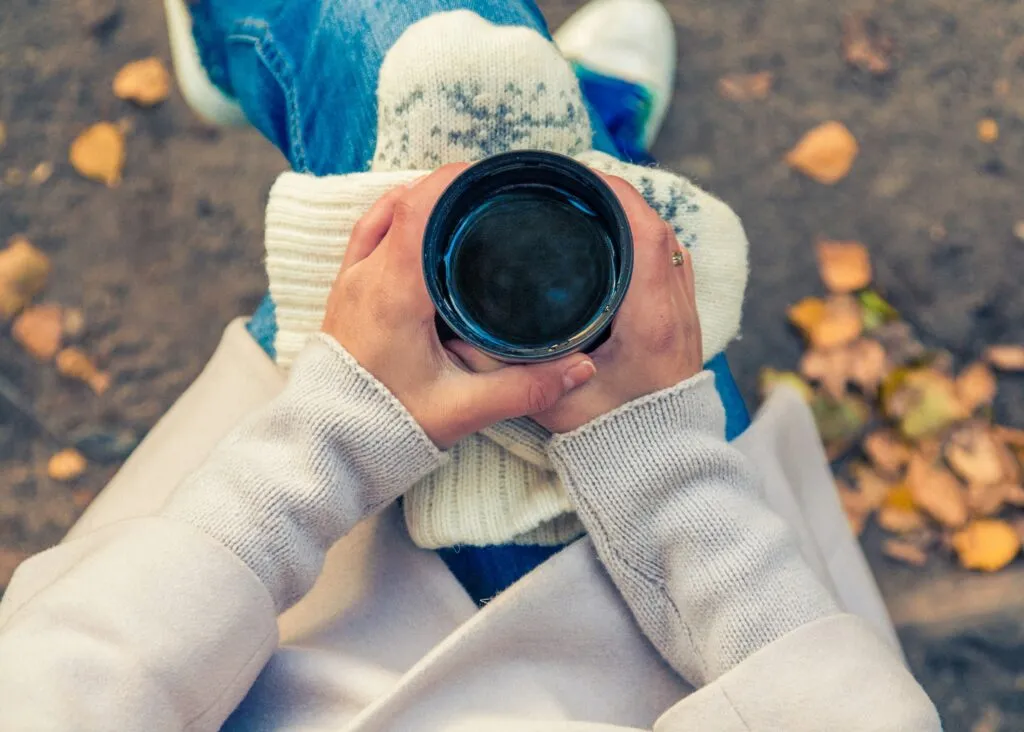 Someone sitting on a bench with a coffee, surrounded by autumn leaves