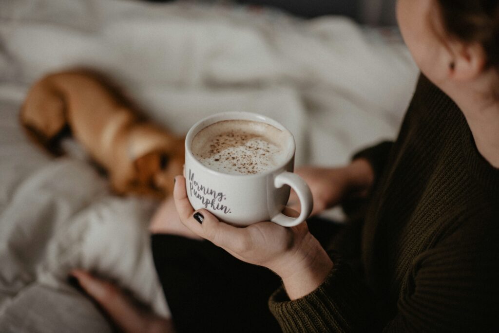 Hands holding a mug of coffee with a dog sleeping in the background