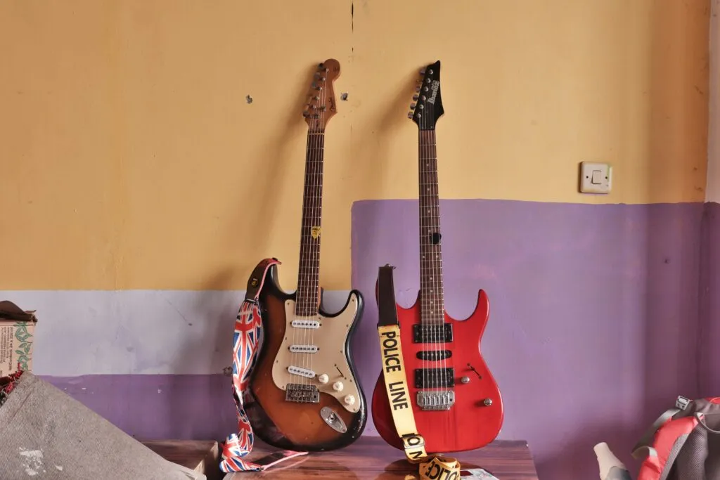 Two guitars sitting again a yellow and purple wall