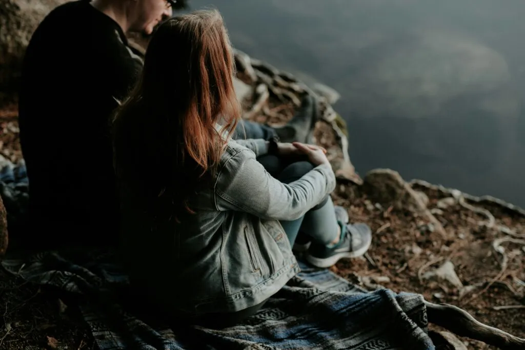 A couple sits on top of a rocky surface, overlooking a mountain view