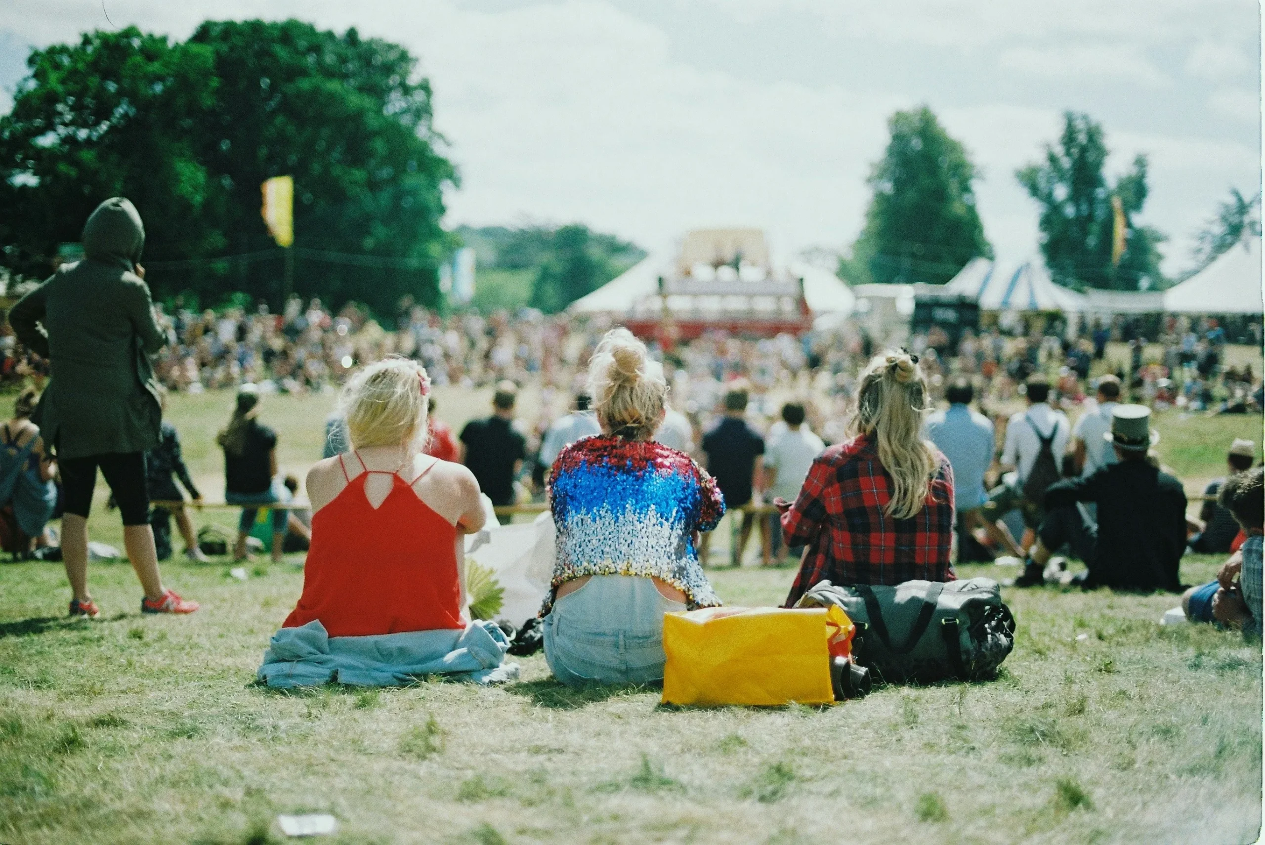 Three women sit on the grass among a crowd of people at a spring festival