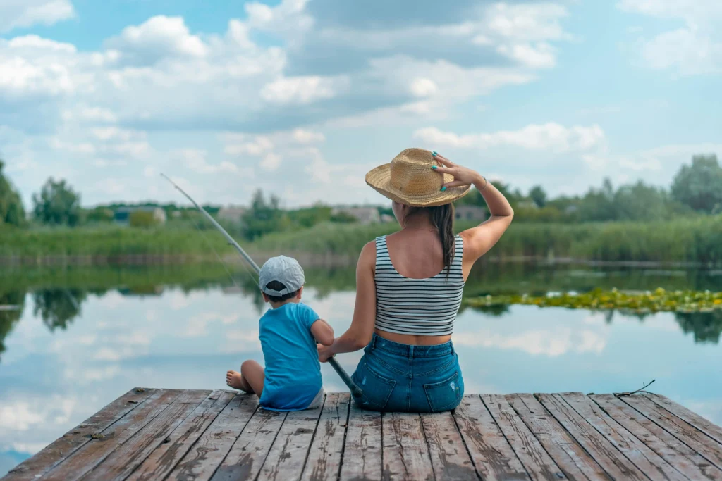 A woman and child sit on a warf while fishing together