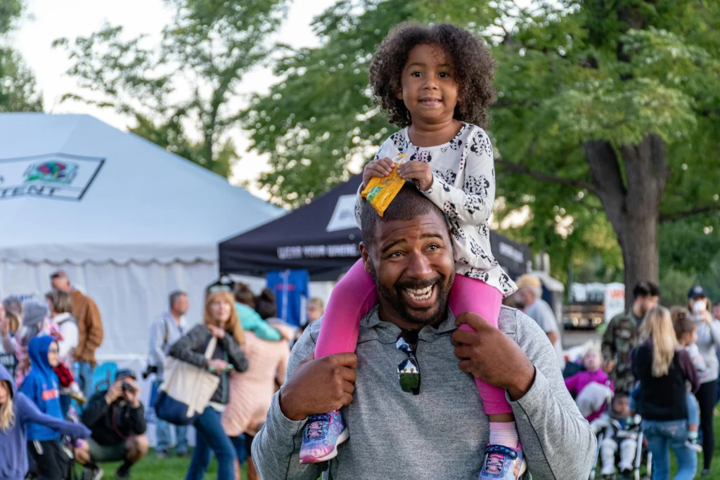 A dad holding his young daughter on his shoulders, both smiling while enjoy creative fathers day ideas and activities