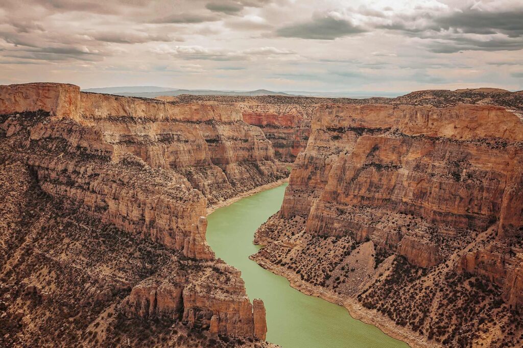 Aerial view of Big Horn Canyon with dramatic sandstone cliffs and a winding green river beneath a cloudy sky