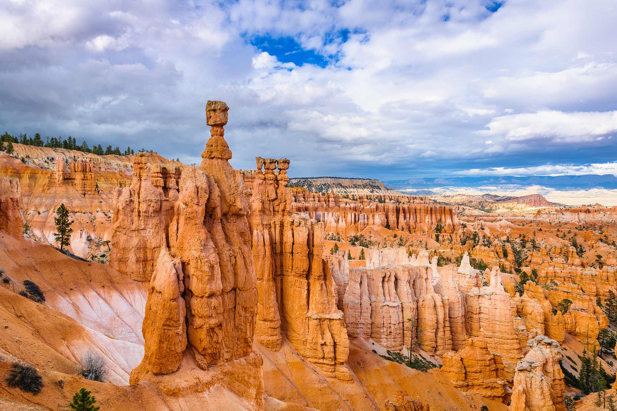 Colorful hoodoos and dramatic sandstone formations at Thor’s Hammer in Bryce Canyon National Park, with vibrant orange cliffs under a partly cloudy sky.