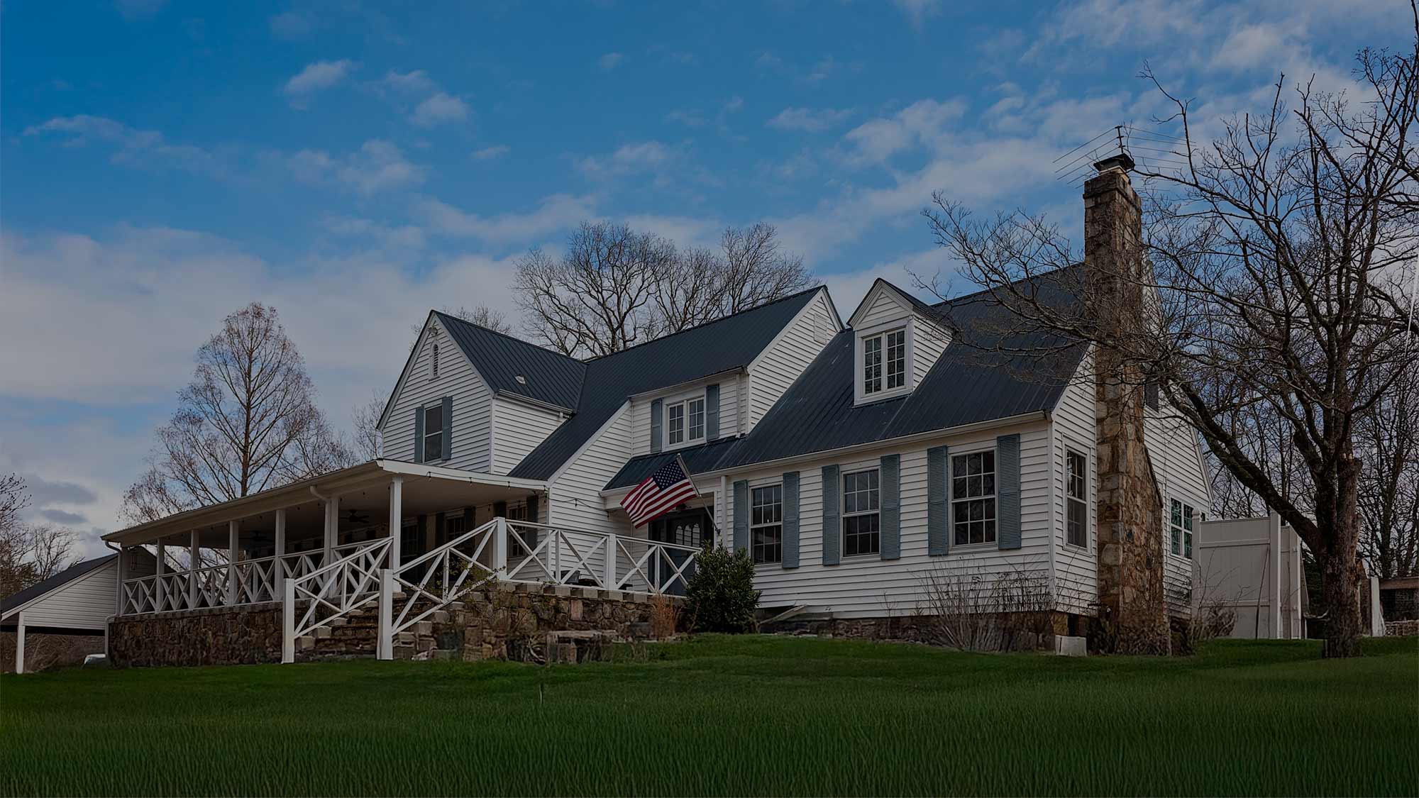 The main white farmhouse at Quail Run Farms in Chattanooga, Tennessee, featuring a wraparound porch, stone chimney, and American flag.