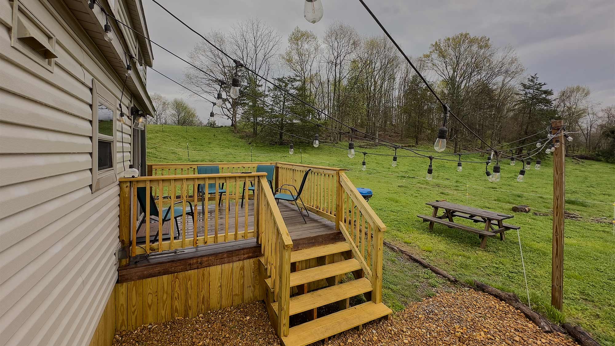 Outdoor deck of a tiny home at Quail Run Farms with string lights, patio seating, and picnic table overlooking the grassy fields.