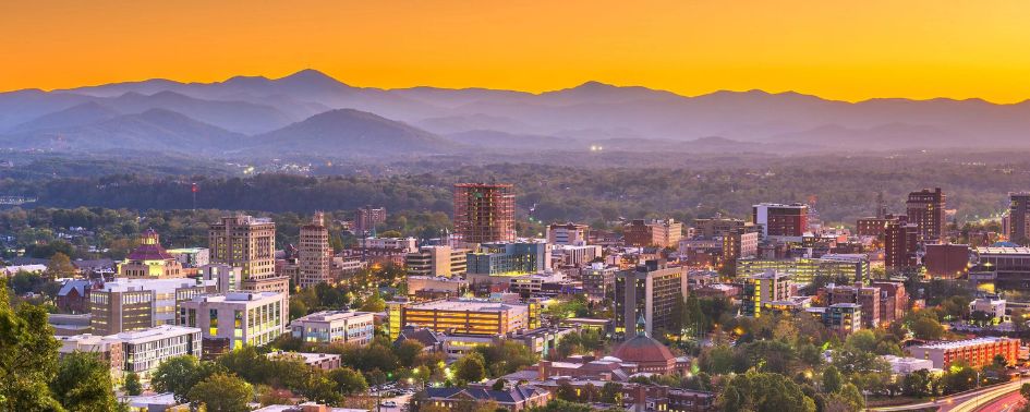 Downtown Asheville, North Carolina skyline with city buildings and Blue Ridge Mountains at sunset.
