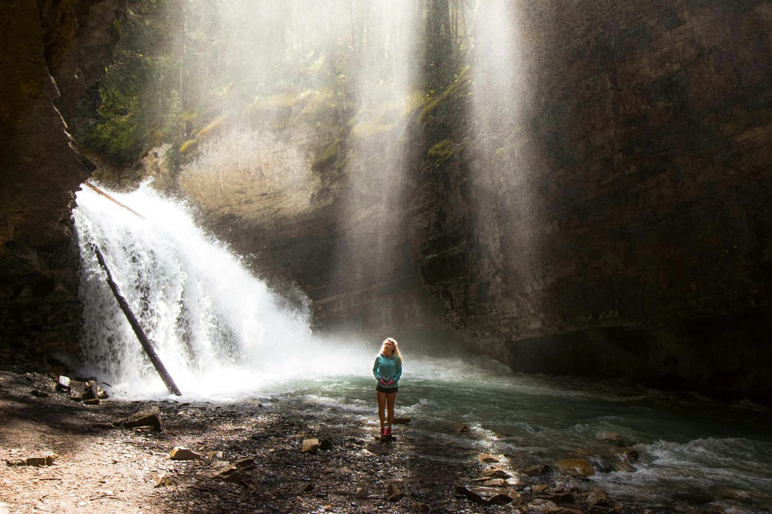 Girl standing beneath a waterfall in Nantahala National Forest, North Carolina, surrounded by rocky canyon walls and misty sunlight
