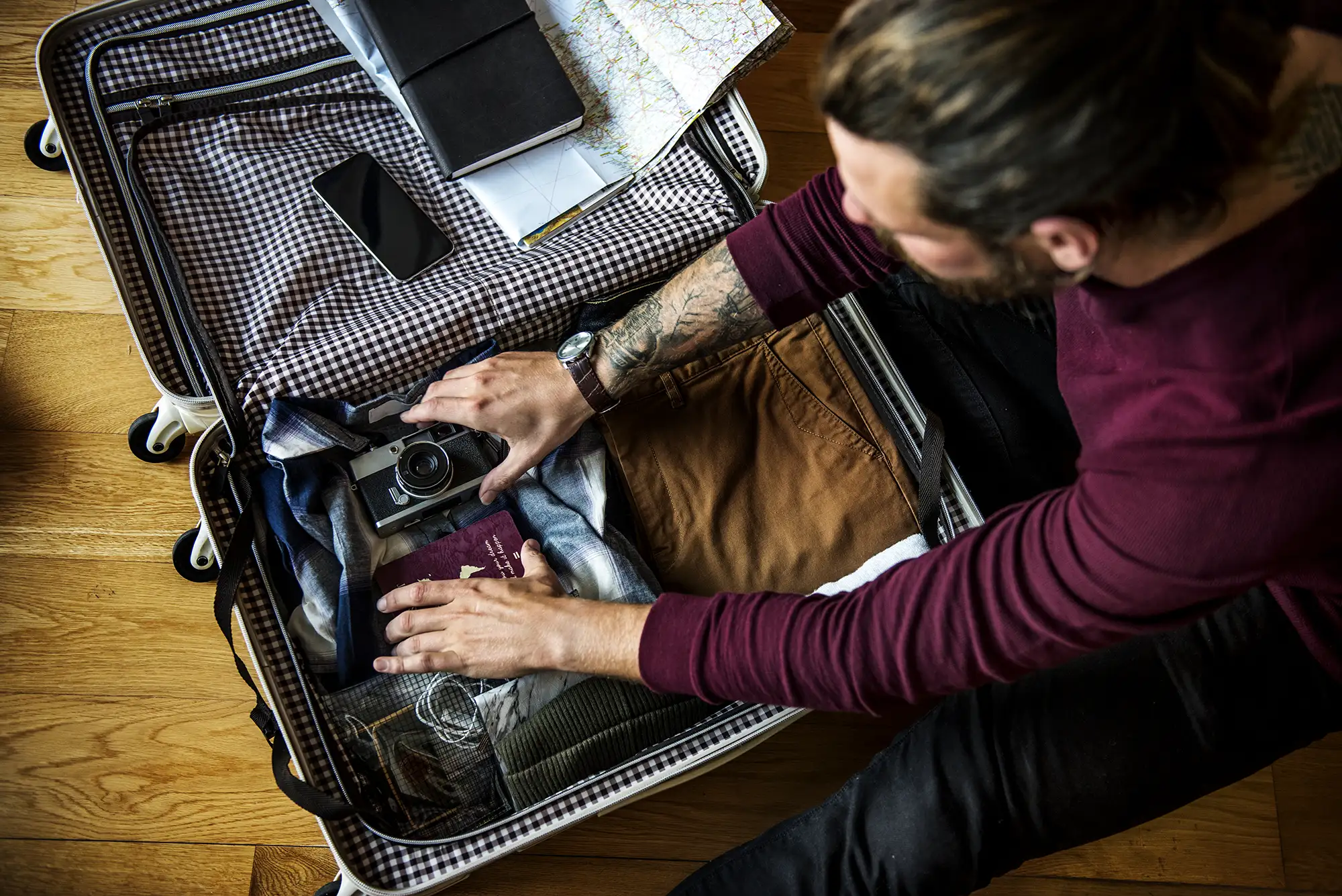 Man packing a suitcase with clothes, camera, passport, and travel essentials