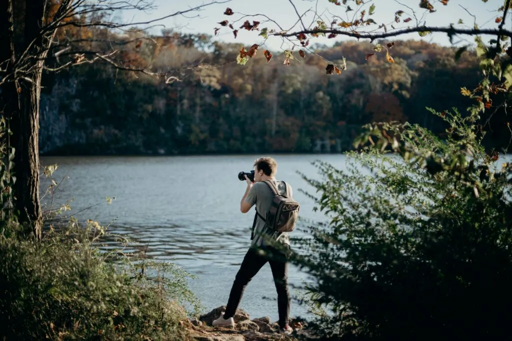 Photographer standing by a lake taking pictures in a natural outdoor setting